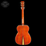 The back of an acoustic guitar with a vibrant, glossy reddish-orange flamed wood finish, shown against a solid black background with a Tone Shop watermark in the top left corner.