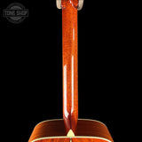 Close-up of the neck and lower body of an acoustic guitar with a glossy reddish-brown wood finish, shown against a solid black background. A Tone Shop watermark is visible in the top-left corner.