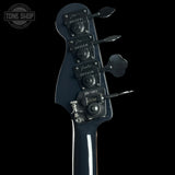 Close-up of the headstock of a Fender bass guitar against a black background, showing the glossy dark blue finish, four tuning pegs, and tuning machines. A Tone Shop watermark is visible in the top left corner.