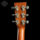 Close-up of the headstock of an acoustic guitar, showing six tuning pegs with silver metal bodies and gold-toned centers on a rich reddish-brown wood finish, set against a solid black background.