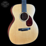 An acoustic guitar with a natural wood top and dark reddish-brown sides, shown against a solid black background. A Tone Shop watermark is visible in the upper left corner.