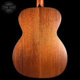 Close-up of the back of a wooden acoustic guitar showing the rich grain of a mahogany or rosewood backplate, set against a solid black background with a Tone Shop logo in the top left corner.
