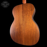 Close-up of the back of an acoustic guitar showing a rich, warm brown wood grain finish, set against a solid black background with a Tone Shop watermark in the upper left.