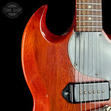 Close-up of a double-cutaway electric guitar body in a glossy reddish-brown sunburst finish, showing part of the silver pickguard, black pickups, and fretboard against a black background.