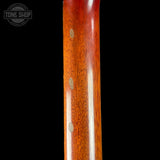 Close-up of a polished reddish-brown wooden instrument body or neck with visible wood grain and small circular inlays, shown against a black background. A Tone Shop watermark appears in the upper left corner.