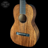 A close-up studio shot of a wooden acoustic guitar body against a solid black background, with a Tone Shop watermark in the upper left corner.