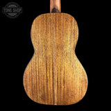 The back of a wooden ukulele or small guitar, showing a rich warm brown wood grain finish, centered against a solid black background with a Tone Shop watermark in the top left corner.