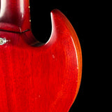 Close-up of a glossy red electric guitar body with a dark cutaway shape, showing the wood grain and a small silver screw against a black background.