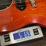 A close-up of a digital scale weighing a portion of a glossy reddish-brown electric guitar. The scale displays 5.