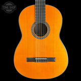 A classic acoustic guitar with a bright orange-yellow spruce top, black headstock, and decorative rosette, shown against a solid black background with a Tone Shop watermark in the top left corner.