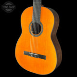 A classical acoustic guitar with a vibrant orange-yellow spruce top and dark brown sides, shown against a solid black background with a Tone Shop watermark in the top left corner.