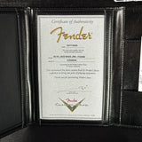A close-up of a black leather Fender instrument certificate holder displaying a silver Certificate of Authenticity insert with gold and red Fender branding.