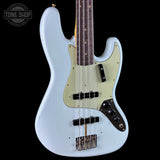 A light blue electric bass guitar with a cream-colored pickguard, dark brown fretboard, and black hardware, shown against a solid black background. A Tone Shop logo is visible in the top-left corner.