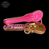 A gold electric guitar resting inside an open vintage pink-lined hard case on a black background, with a Tone Shop watermark in the top left corner.