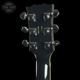 Close-up of a guitar headstock with tuning pegs on a black background, featuring 'Tone Shop' branding.