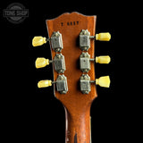 Close-up of the back of a vintage acoustic guitar headstock, showing six yellow tuning pegs, silver tuning machines, and the serial number 76657 on a black background.