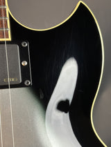 Close-up of a black electric guitar with a white pickguard on a dark background