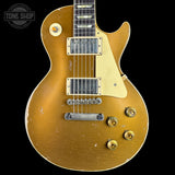 A classic electric guitar with a distressed gold finish, featuring a cream pickguard, dual humbucker pickups, and gold-toned control knobs, shown against a solid black background.