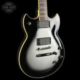 Electric guitar with a silver finish on a black background, featuring the Tone Shop logo.