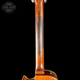 Close-up of the neck of a vintage electric guitar, showing a heavily worn and chipped maple headstock with a glossy orange-brown finish, set against a solid black background.