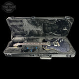 A used electric guitar with a dark blue flamed maple top and gold hardware, resting inside an open black hard case on a black background. A Tone Shop logo is visible in the top left corner.
