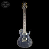 A Gibson electric guitar with a blue flamed maple top and a dark, glossy blue-gray finish, shown against a solid black background. The headstock features gold hardware and a Tune Shop watermark is visible in the upper left corner.