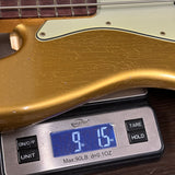 A close-up of a gold-finished electric bass guitar body resting on a digital scale displaying its weight in ounces.