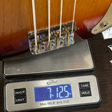 A close-up of a guitar bridge and tailpiece assembly resting on a digital scale, showing a weight reading of 7.125 oz.