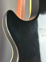 Close-up of a guitar's body with a focus on the black finish and wood grain.