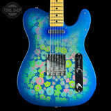 A blue electric guitar with a vibrant pink, green, and blue floral pattern on the body, shown against a solid black background. The neck is a natural maple wood color with black frets.