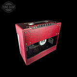 A red textured speaker amplifier with a glass front window, showcasing the internal speaker and control knobs, set against a solid black background.