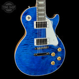 A blue flamed maple electric guitar with a white pickguard, gold hardware, and a black background. A Tone Shop watermark is visible in the top left corner.