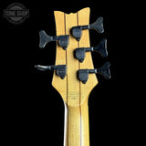 Close-up of a bass guitar headstock with tuning pegs on a black background, featuring the Tone Shop logo.