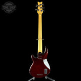 Red electric bass guitar on a stand with 'Tone Shop' logo in the corner.