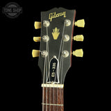 Close-up of a Gibson ES-335 electric guitar headstock, showing the black headstock with gold Gibson script, a gold crown logo, six tuning pegs, and the model number ES-335. The neck has a dark brown wood fretboard and white binding, set against a solid black background.