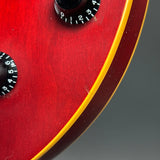Close-up of a red electric guitar body with black control knobs and a gold binding edge, photographed against a dark gray background.