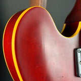 Close-up of the back of a red electric guitar body with a yellow edge stripe, showing wood grain, a vertical scratch, and part of the pickup assembly against a dark background.