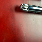 A close-up detail shot of a silver metal guitar bridge and strings resting on a red wooden surface.