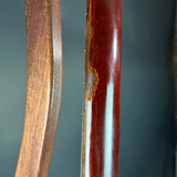 Close-up of two wooden curved objects, likely furniture legs or trim, showing a glossy dark reddish-brown wood finish with visible grain and a small worn area on the right piece.