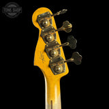 Close-up of the headstock of a vintage electric bass guitar, showing a yellow-orange maple wood finish, four gold-toned tuning pegs, and a Tone Shop logo watermark in the upper left corner against a solid black background.