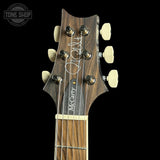 Close-up of the headstock of a McCarty guitar against a black background, showing the dark wood grain, six cream-colored tuning pegs, and the McCarty brand name printed vertically on the headstock.
