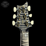 Close-up of the headstock of a guitar, showing six white tuning pegs, gold-toned tuning screws, and gold lettering on a black background. A Tone Shop watermark is visible in the top left corner.