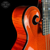 Close-up of a glossy orange-red electric guitar body with a fluted cutaway and black binding, shown against a black background. Part of the fretboard and strings are visible.
