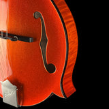 Close-up of a glossy orange-red f-hole guitar body with a glitter finish, black soundhole surround, and part of the bridge visible against a black background.