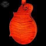 Close-up of the back of a mandolin with a vibrant orange-red flamed maple wood finish, set against a solid black background. A Tone Shop watermark is visible in the top-left corner.