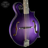A purple mandolin with a metallic glitter finish, shown from the front against a solid black background. The mandolin features a decorative scroll on the headstock, f-holes, and a silver metal bridge and tailpiece.