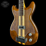 Wooden electric bass guitar with a black background, featuring the Tone Shop logo.