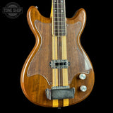 Wooden electric bass guitar with a clear finish on a black background, featuring the Tone Shop logo.