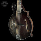A close-up studio shot of a mandolin against a solid black background, featuring a dark brown glitter finish, a natural wood fingerboard, and a Tone Shop watermark in the top left corner.