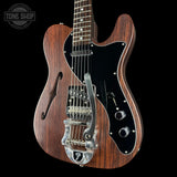 Wooden electric guitar with a black pickguard on a black background, featuring the Tone Shop logo.